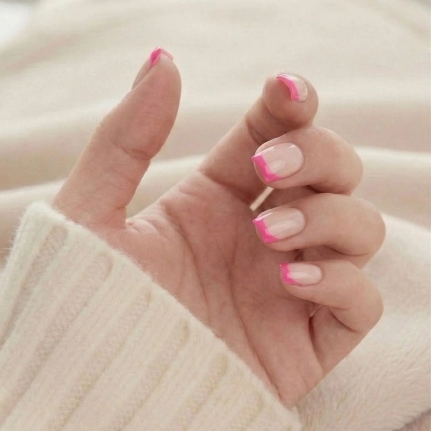 Pixie Pink korte square-løsnegler – rosa fransk spiss sett oppover mot strikket genser