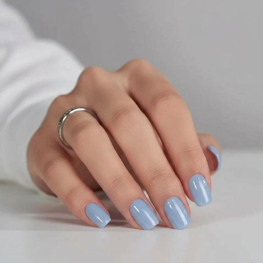 Baby Blue press-on naglar — blank ljusblå fyrkantig manikyr, hand som vilar på vit yta med silverring