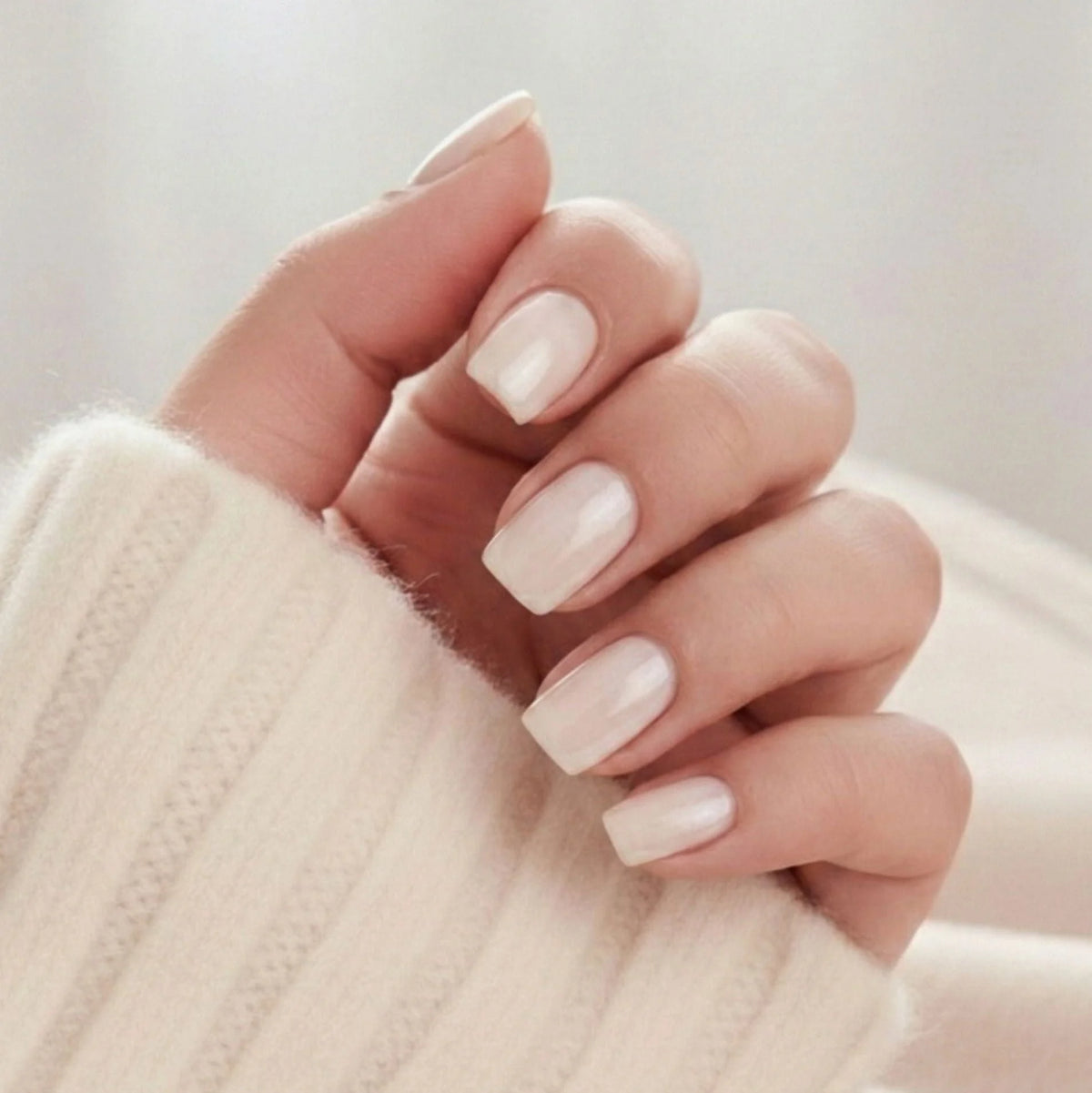 Pure Pearl press-on negler – korte square i nude pearl med skimrende glans mot kremfarget strikket genser
